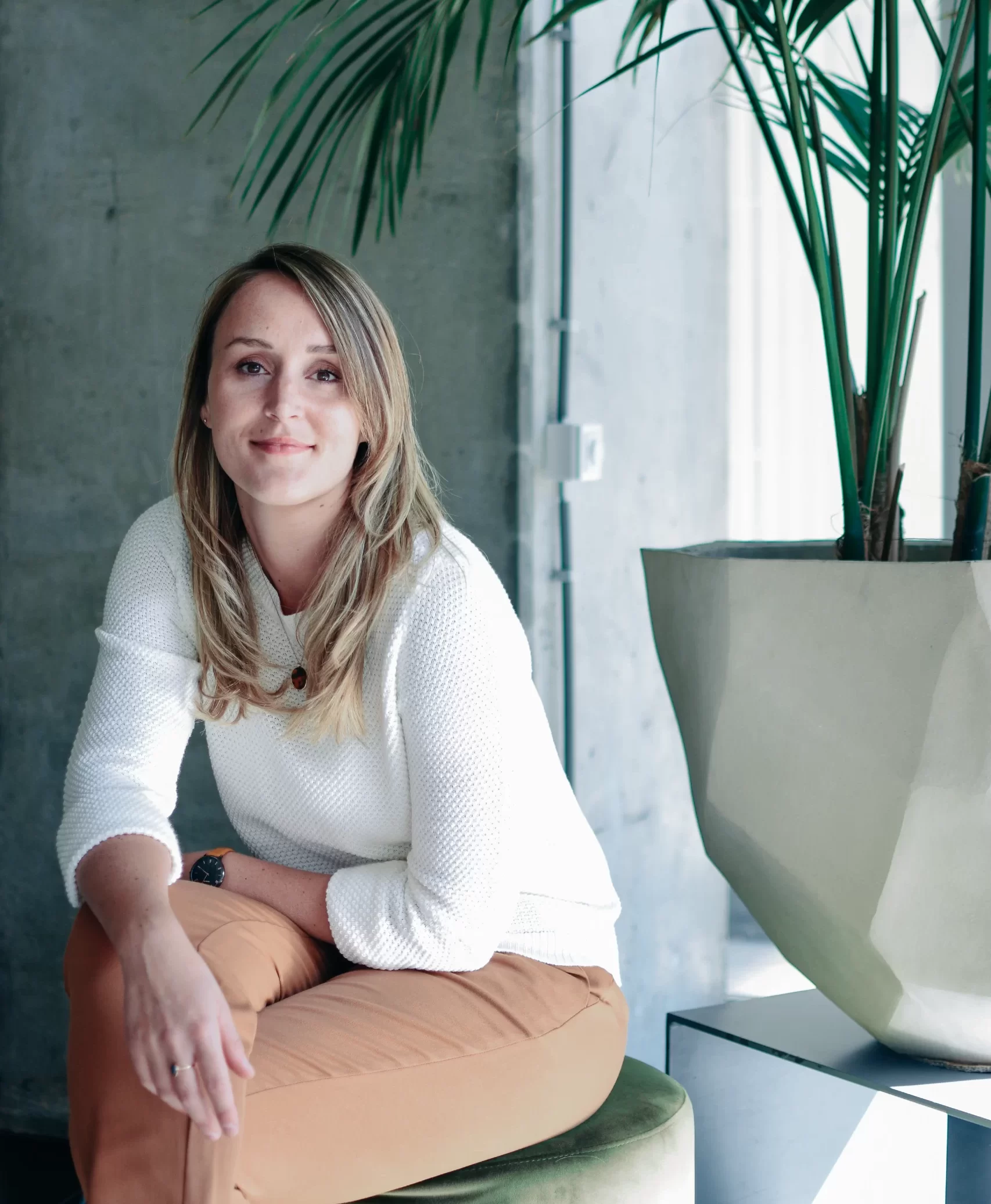 Samantha van Samantics poseert zittend naast een plantenbak. Ze kijkt in de camera.