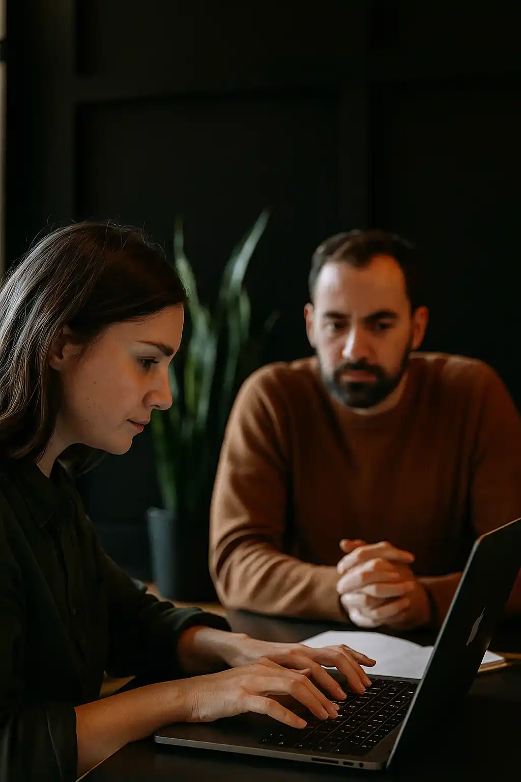 Twee professionals in gesprek aan een tafel in een moderne, warme kantooromgeving. De focus ligt op samenwerking en strategie, met een realistische en mensgerichte sfeer.